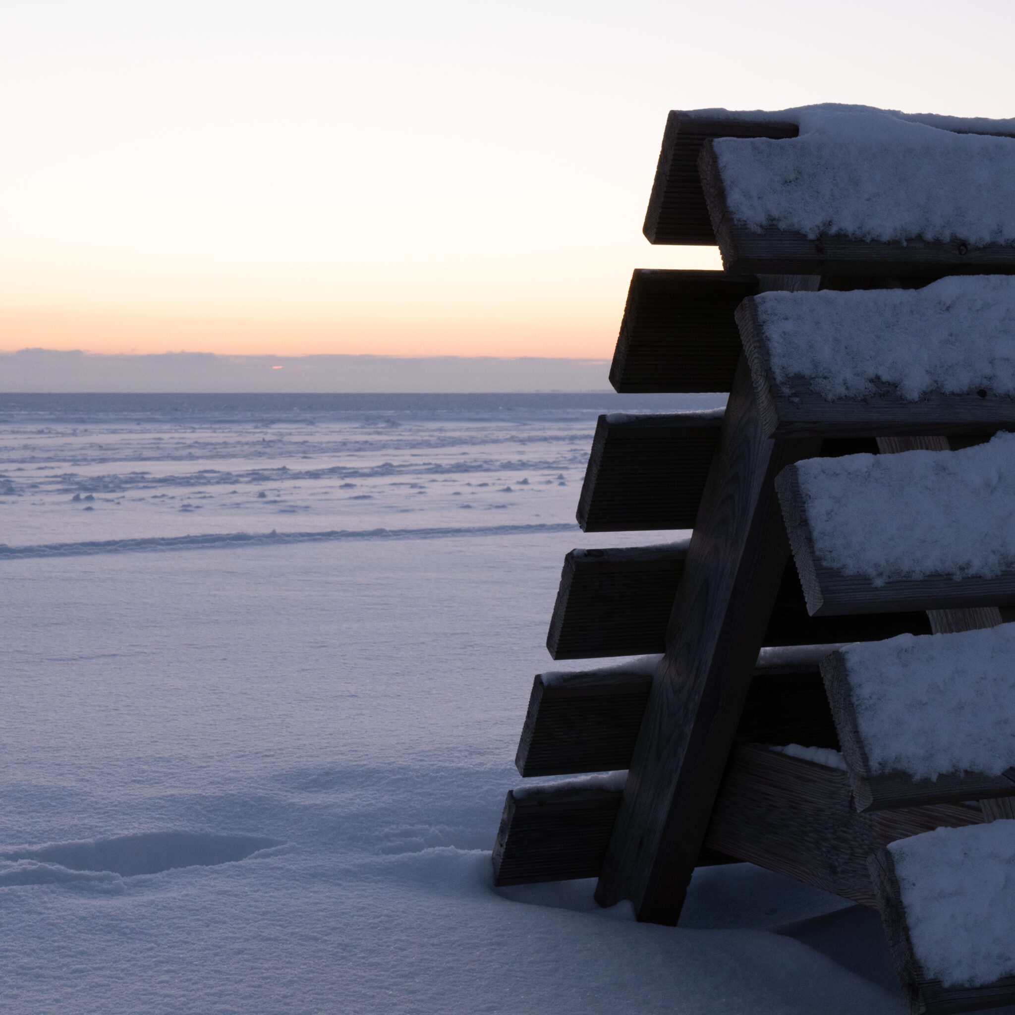Lumega kaetud puidust pink jäätunud järve ääres päikeseloojangul.