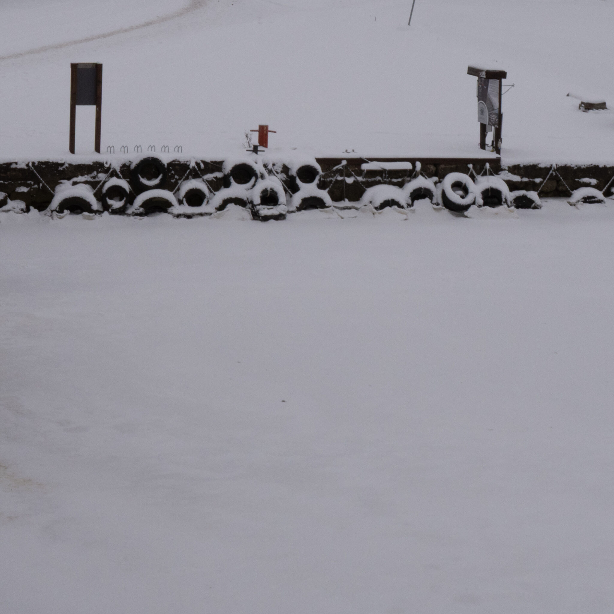 Lumega kaetud rehvid kivimüüri ääres, taustal sildid.