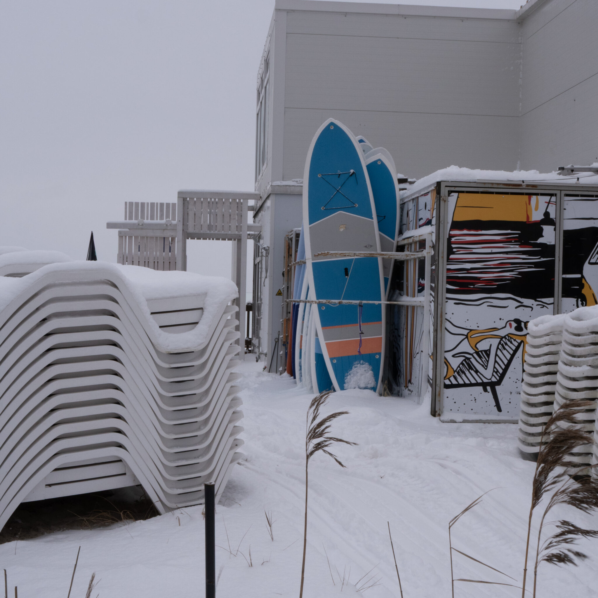 Lumega kaetud rannatoolid ja aerulauad talvises rannamiljöös.