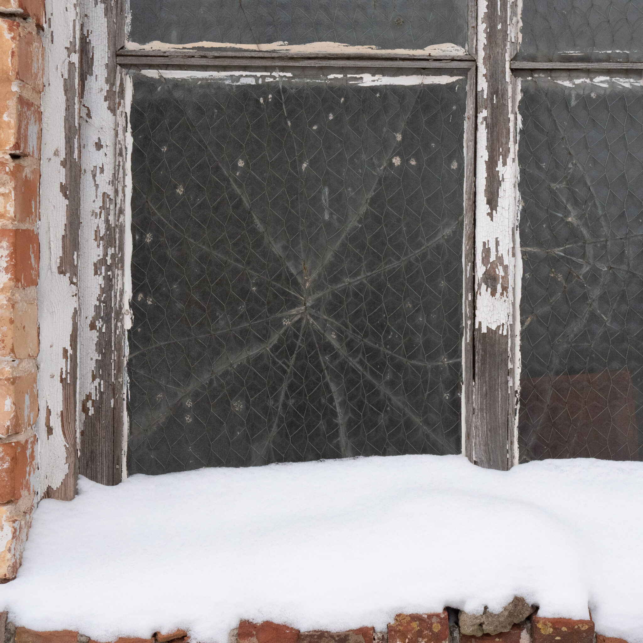 Vana ilmastikunäinud aken kanavõrgu ja lumega maapinnal.