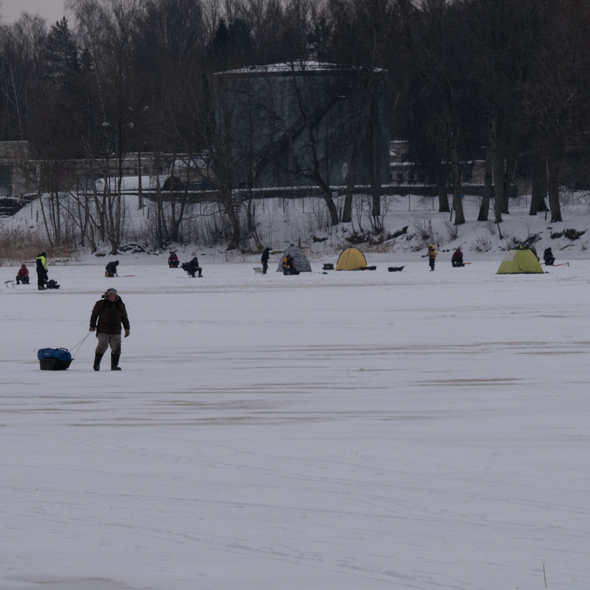 Mees tõmbab kelku jäätunud järvel, taustal telgid ja inimesed.