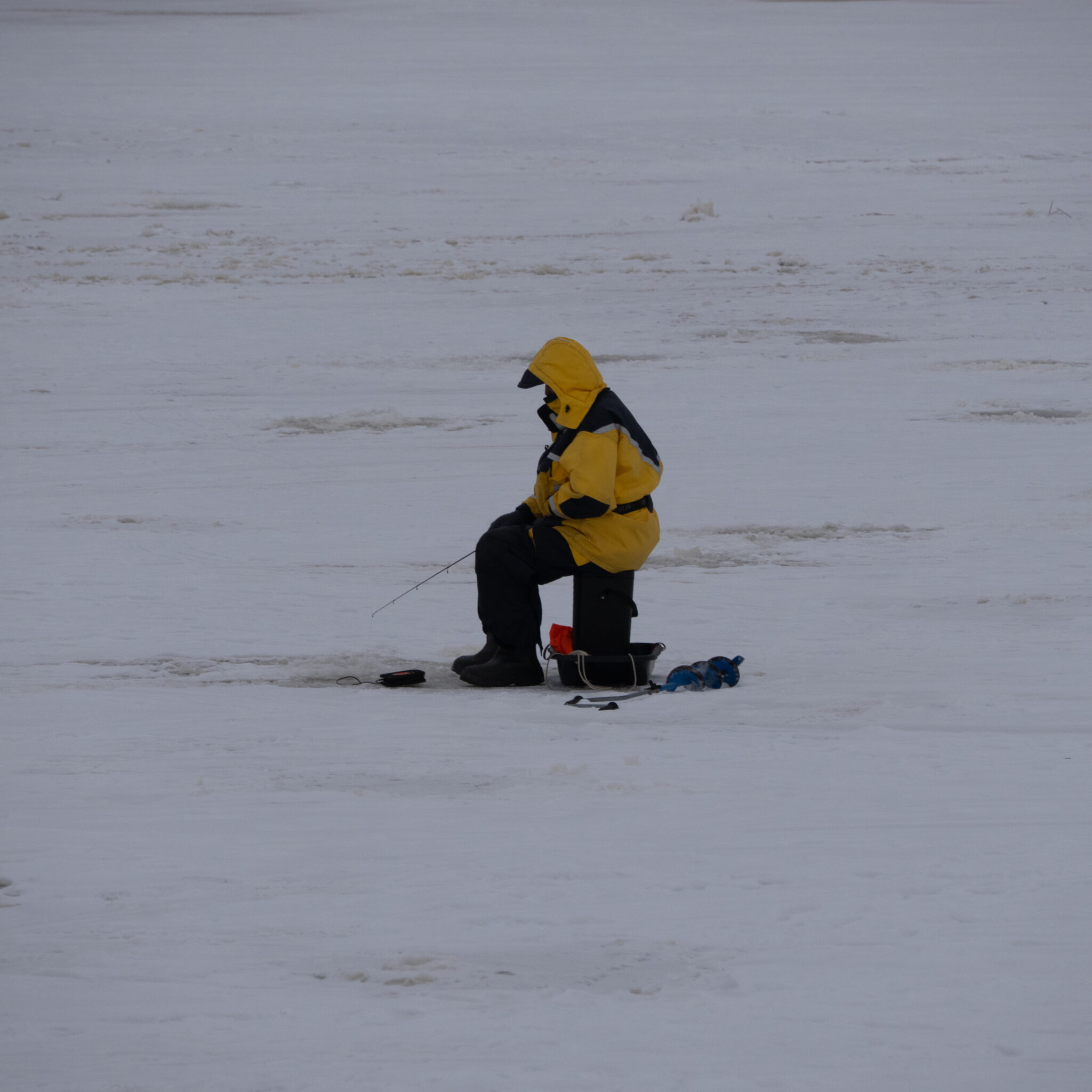 Kollases jopes inimene istub ämbril ja püüab lumes kala.