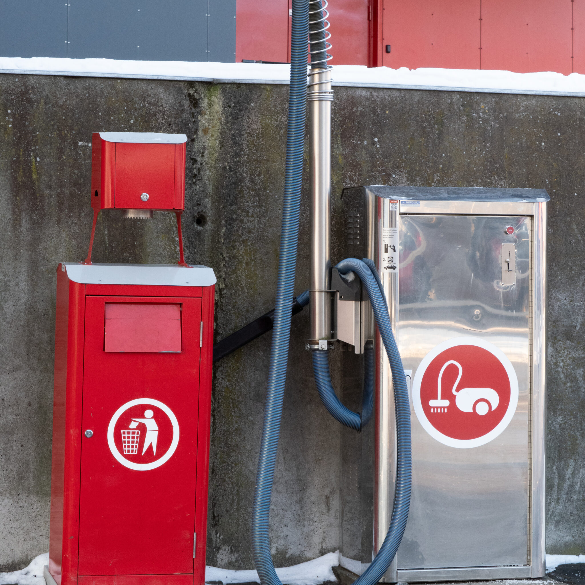 Punane prügikast ja tolmuimeja seina kõrval.