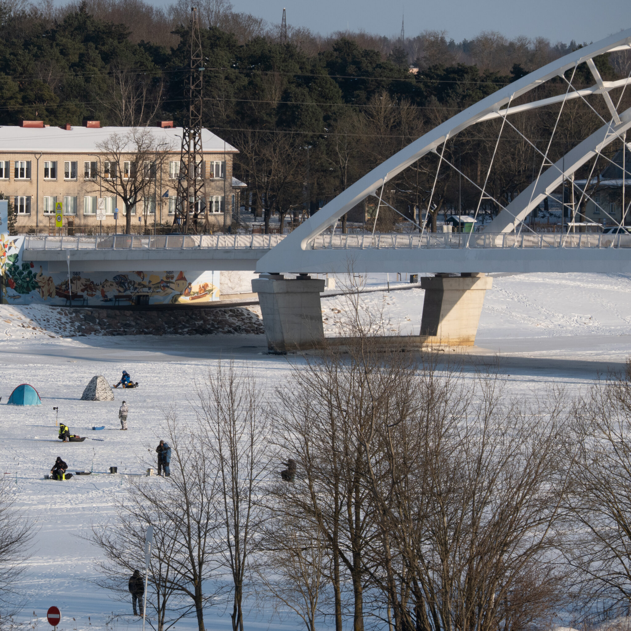 Jääkalastajad jäätunud jõel, taustal sild ja hooned.