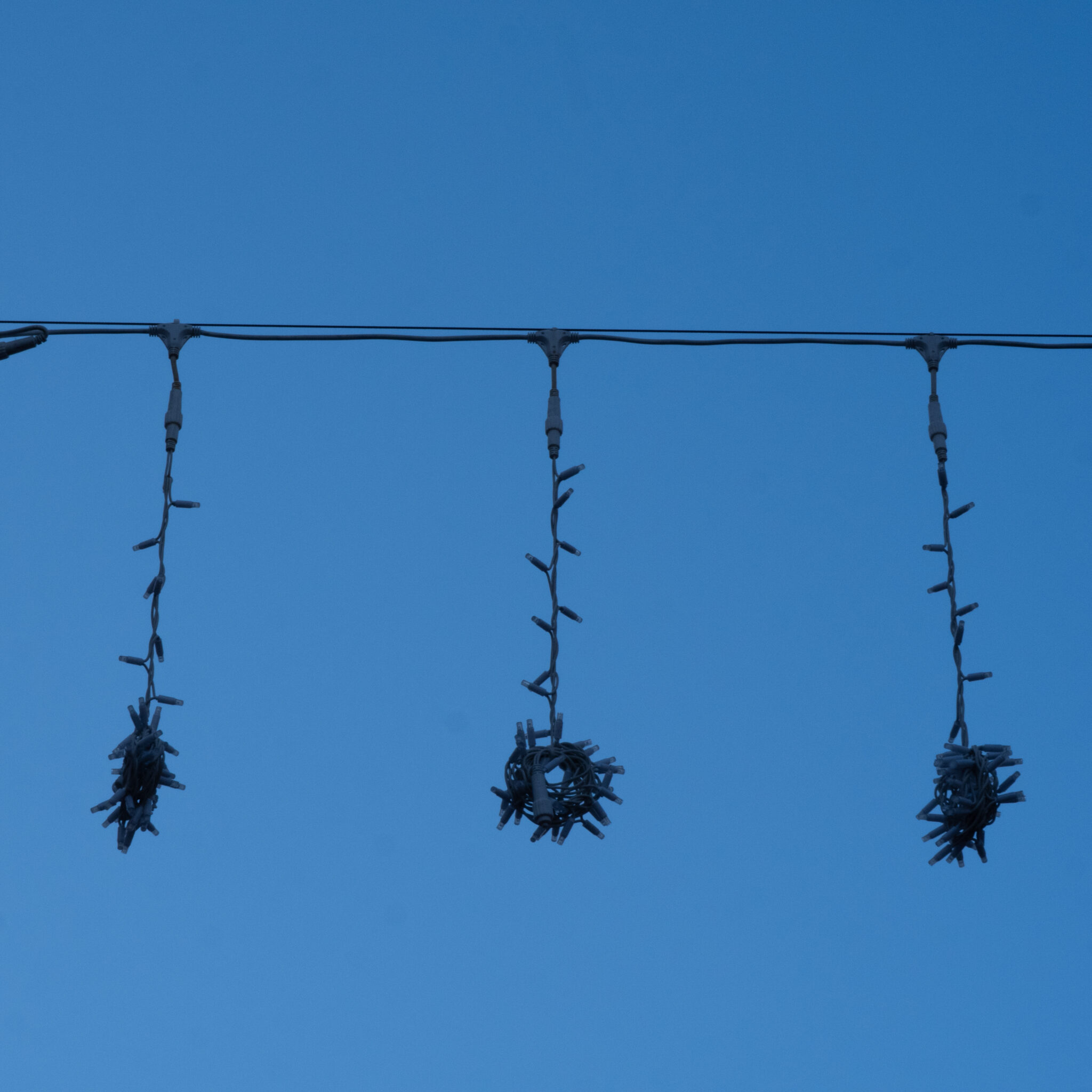 Kolm valgusketti ripuvad juhtme küljes sinise taeva taustal.