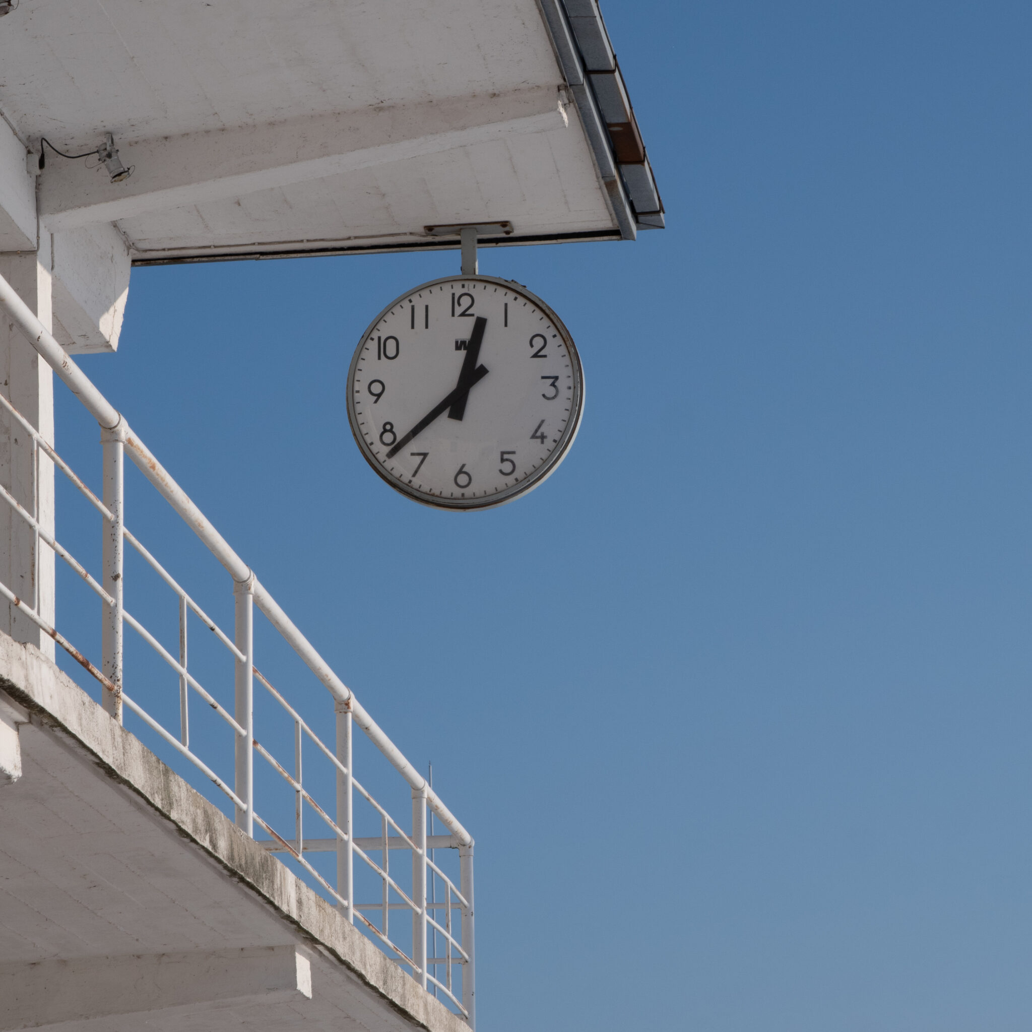 Hoone küljest rippuv kell selge taeva taustal.