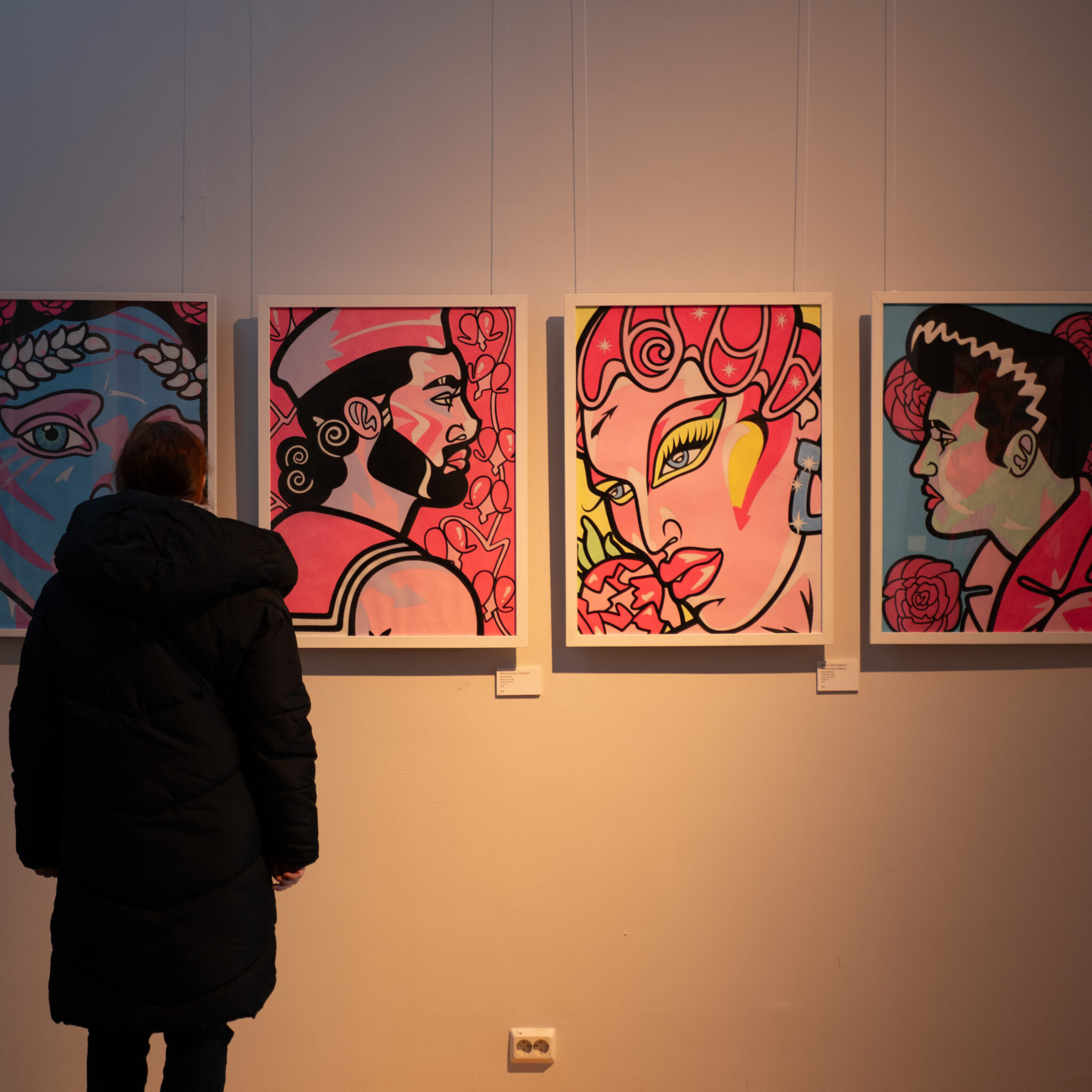 Mustas mantlis naine vaatab seinal olevaid värvilisi maale.