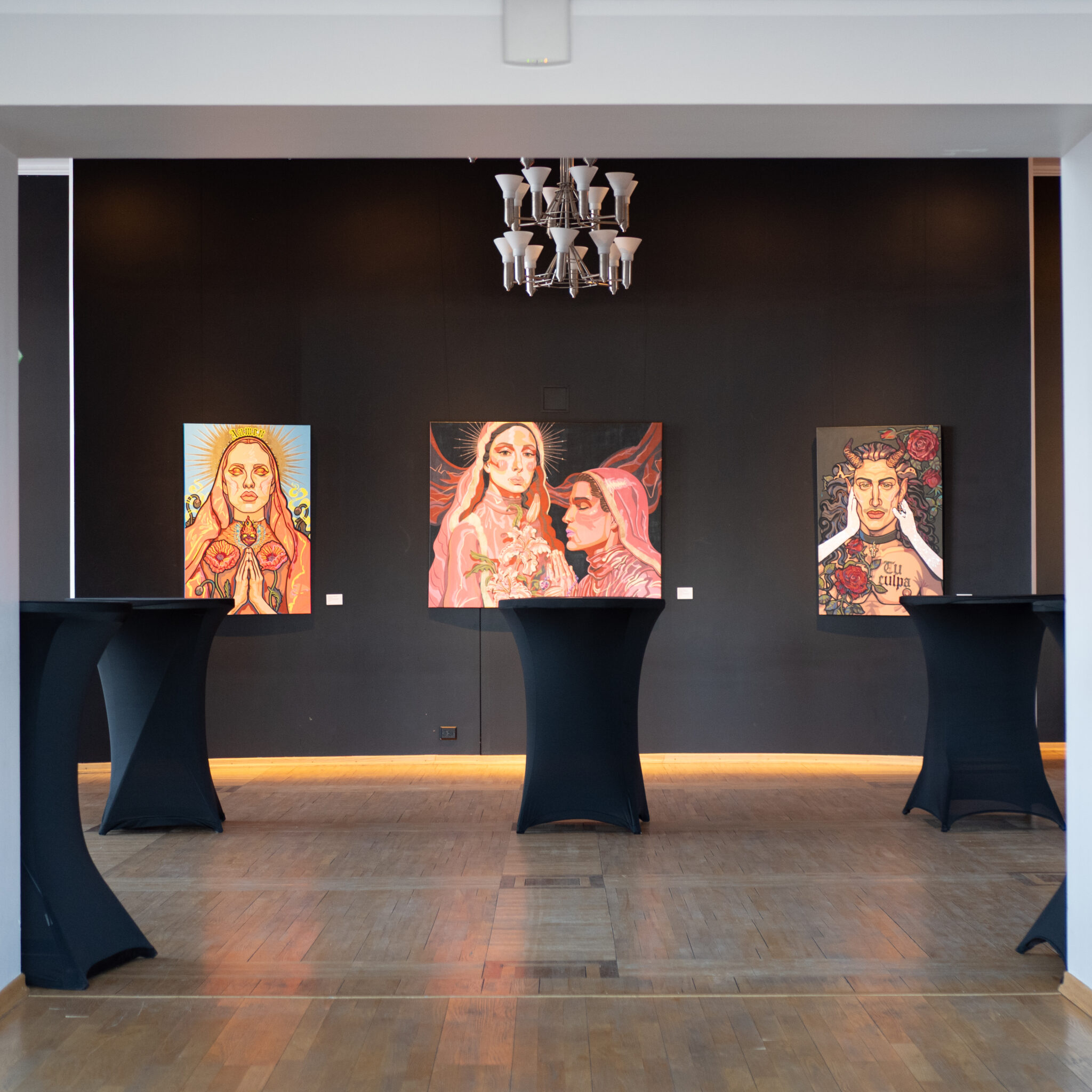 Mustade seinte ja lühtriga kunstigalerii värviliste maalidega.