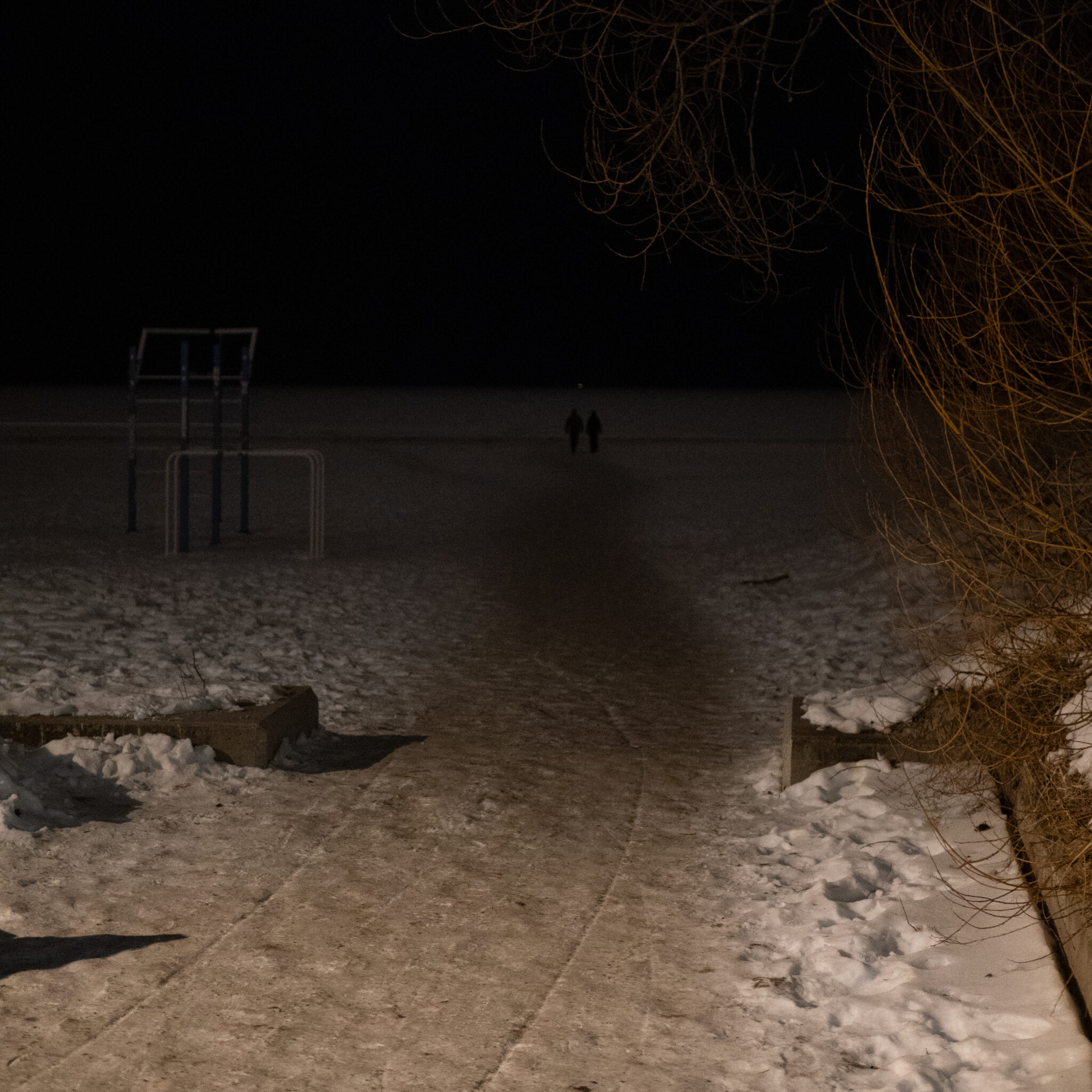 Kaks siluetti kõnnivad öösel lumisel rajal.